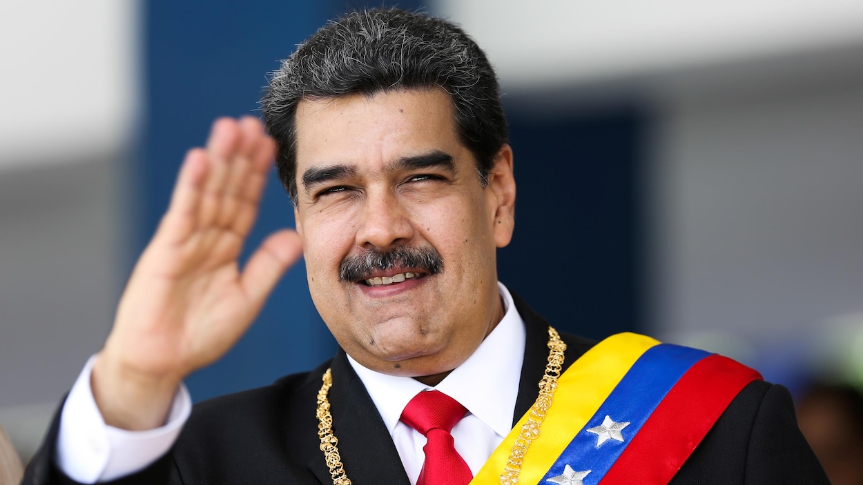 Nicolas Maduro portant une écharpe et un collier et saluant de la main droite