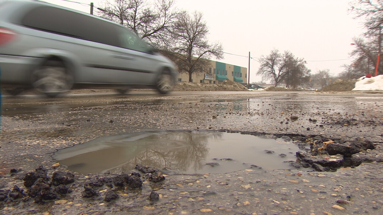 Une voiture roule sur une route endommagée.