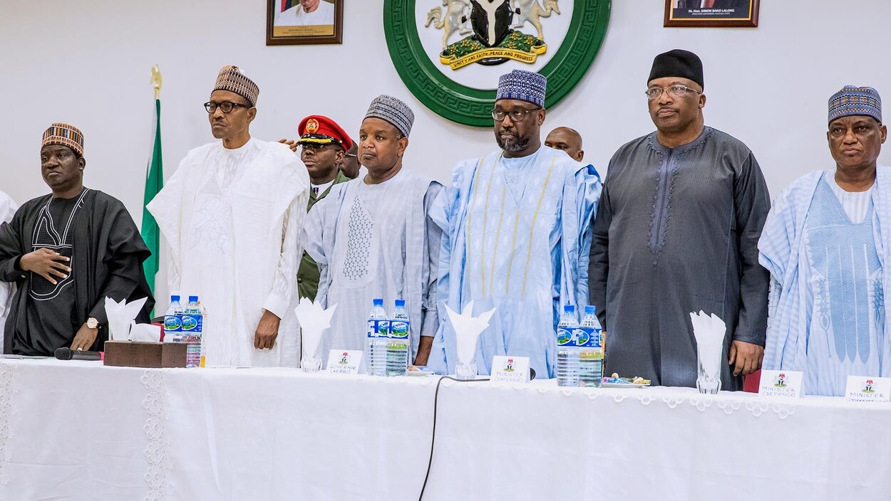 Six dignitaires nigérians lors d'une conférences de presse se tiennent debout derrière une table.