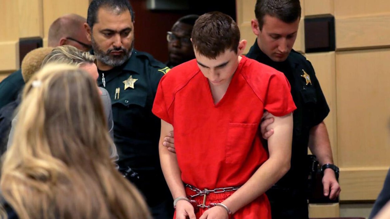 Nikolas Cruz tête baissée entouré de deux agents de la paix Nikolas Cruz tête baissée entouré de deux agents de la paix