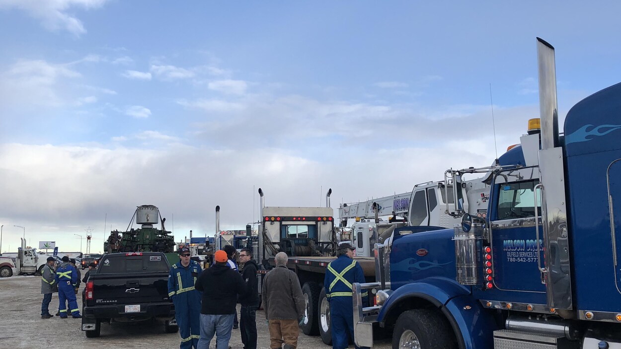 Des camions sont stationnés. Des hommes, dont certains en uniforme bleu, sont debout autour.