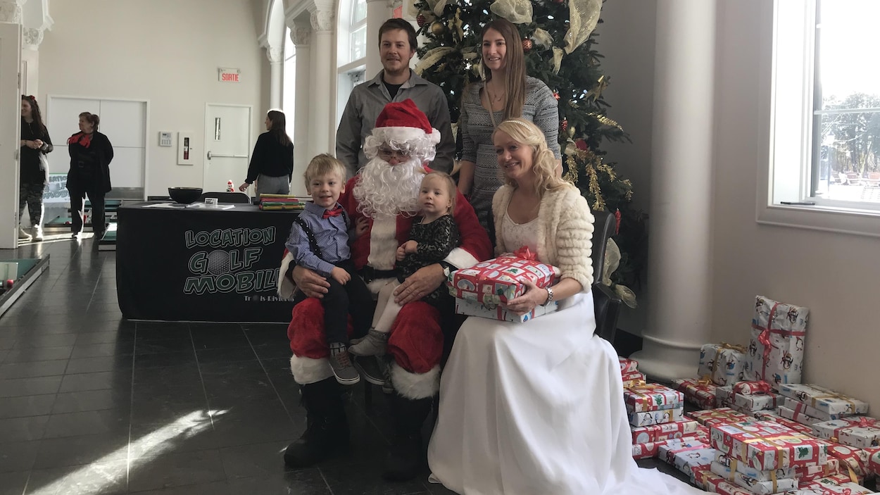Des enfants sur les genoux du père Noël aux côtés d'une femme vêtue en fée des étoiles. Des parents se tiennent debout derrière.