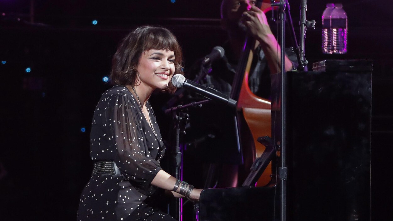 Assise au piano, Norah Jones sourit à la foule.