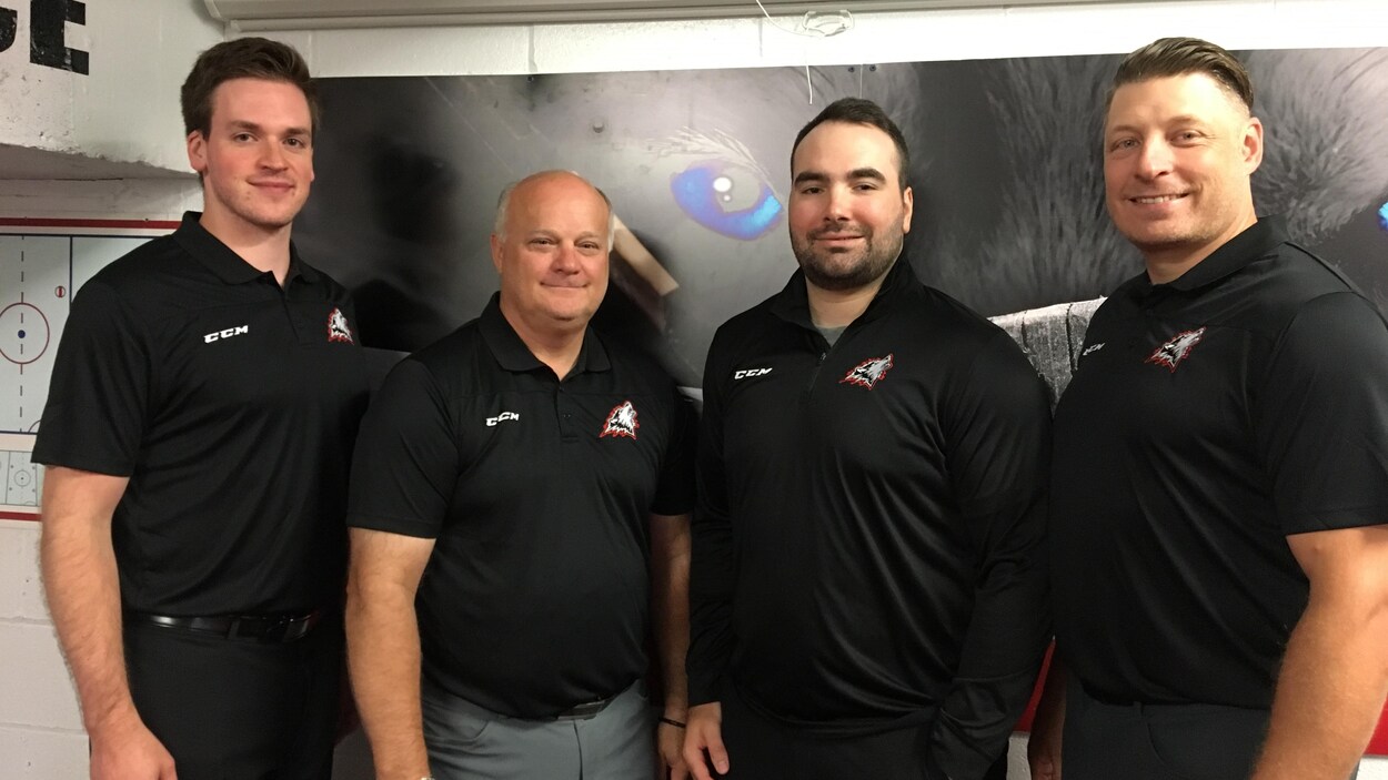 Quatre hommes portant un polo des Huskies de Rouyn-Noranda posent dans l'aréna Iamgold.