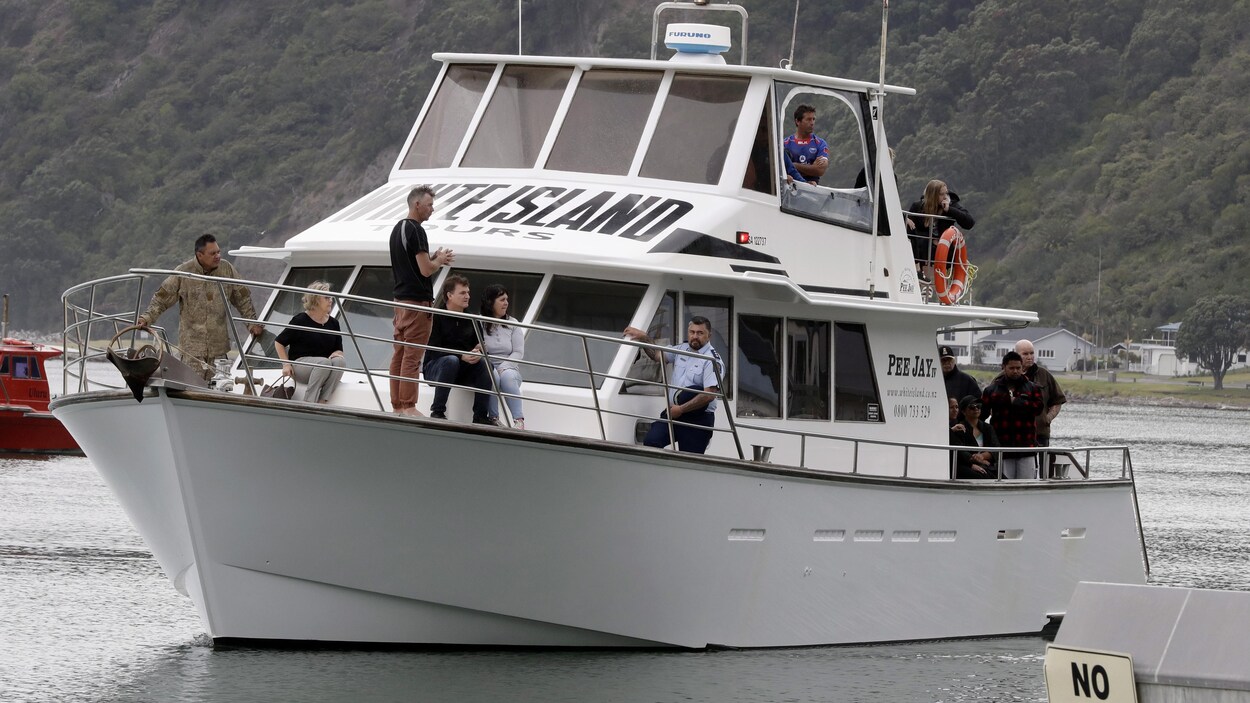 Un bateau sur lequel plusieurs personnes se tiennent debout et assises à l'approche du quai d'embarquement.