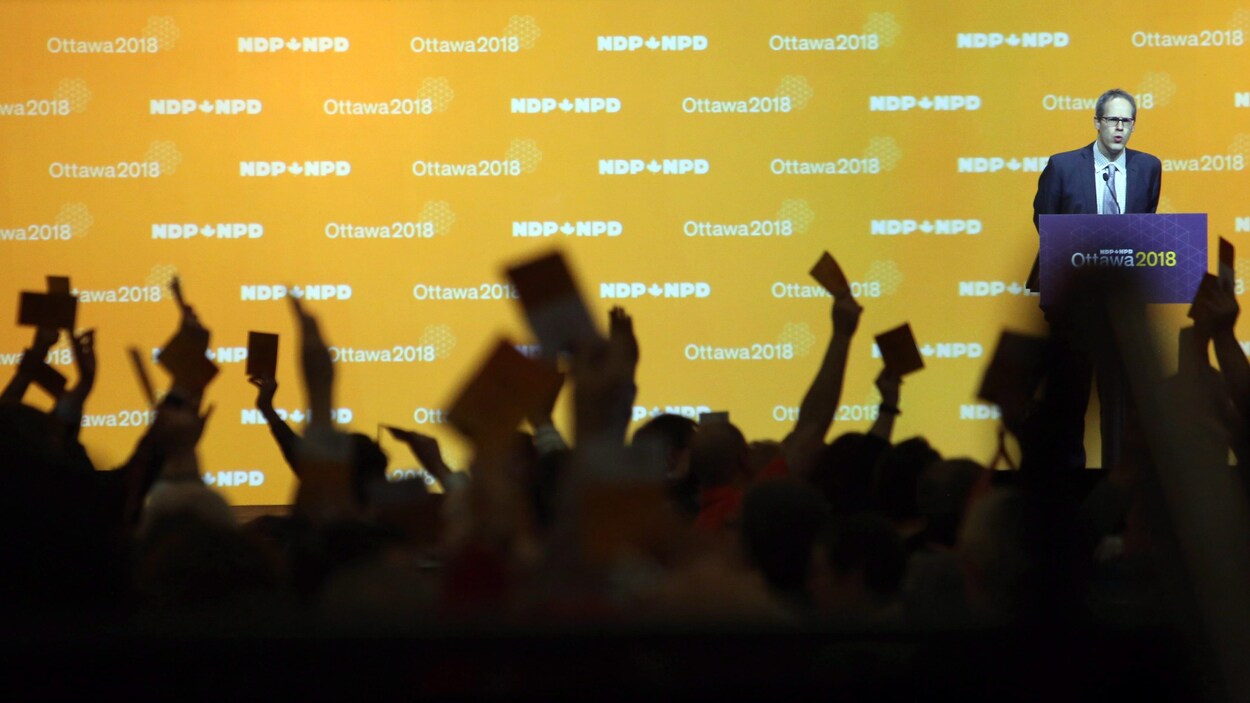 Des mains levées avec un papier et un homme au podium