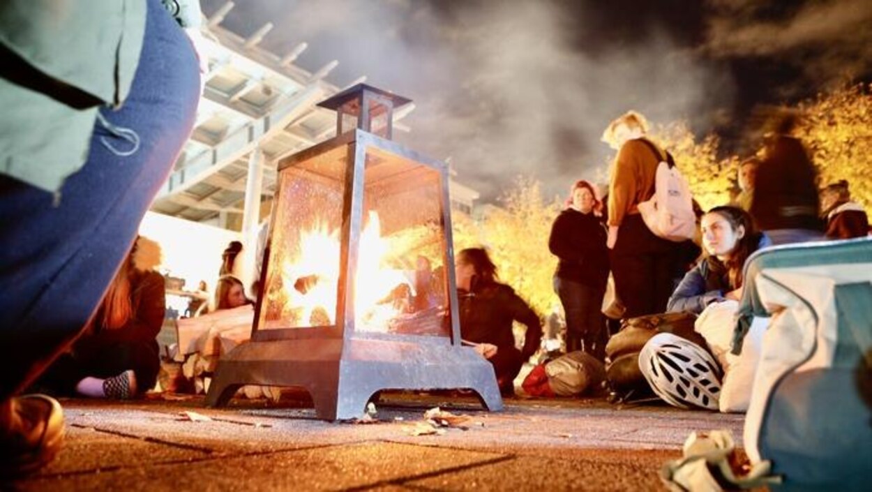 Des gens sont réunis autour d'un feu en ville le soir dans le cadre de la Nuit des sans-abris
