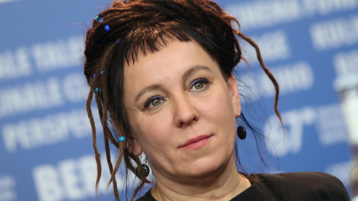 Portrait de Olga Tokarczuk, dont les cheveux sont ornés de perles bleues.