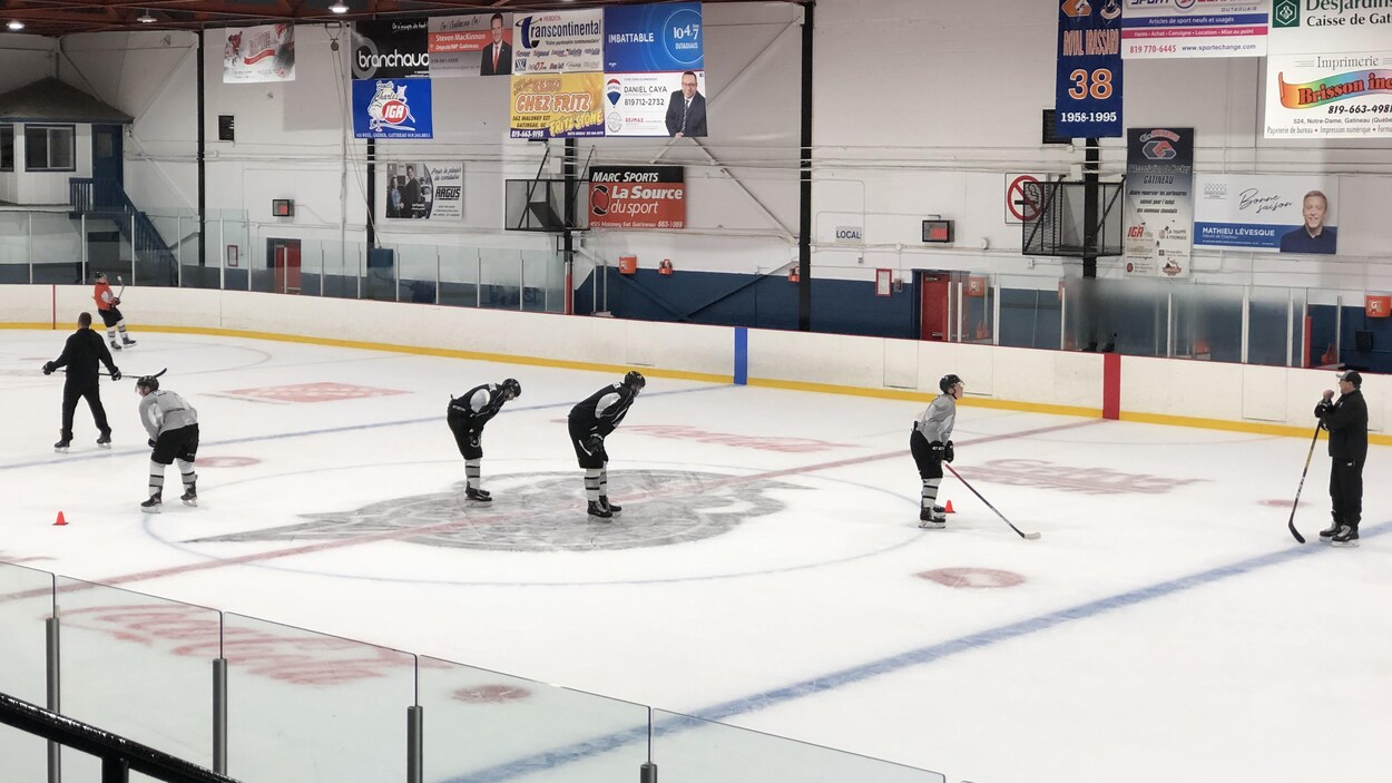 Quatre joueurs de hockey et deux entraîneurs sur la patinoire pendant un entraînement.