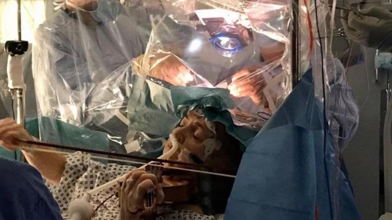 Une femme, allongée, joue du violon pendant que l'équipe médicale opère son cerveau.