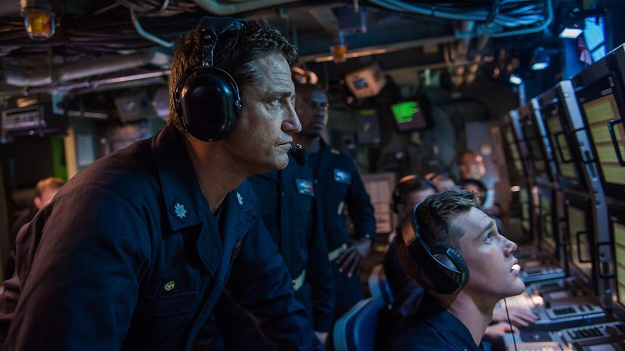 Portant un casque avec un micro, Gerard Butler, de profil, regarde des moniteurs dans une scène du film «Opération Hunter-Killer».