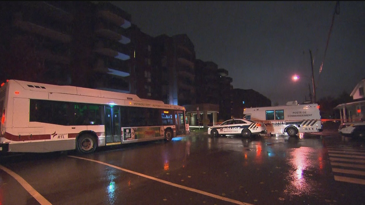 Des véhicules de police et un autobus sont stationnés devant des immeubles à logement.