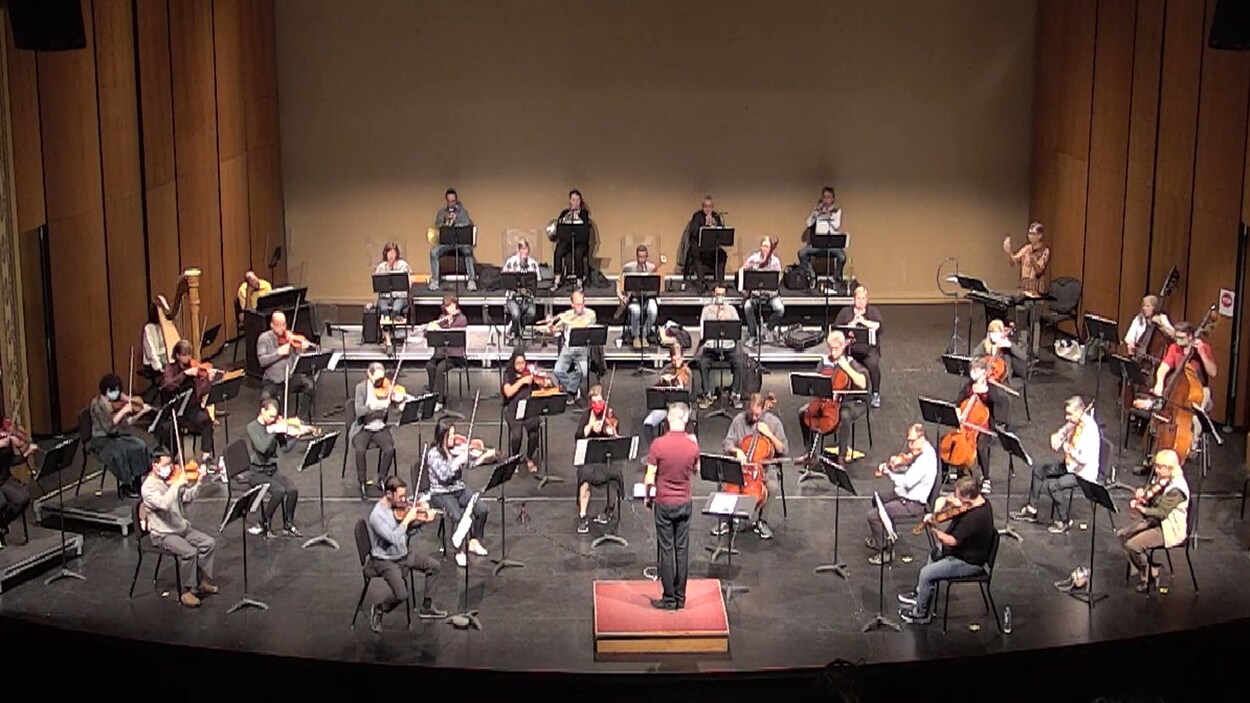 Les musiciens d'un orchestre jouent de leur instrument en portant un masque et en étant plus espacés les uns des autres qu'à l'habitude.
