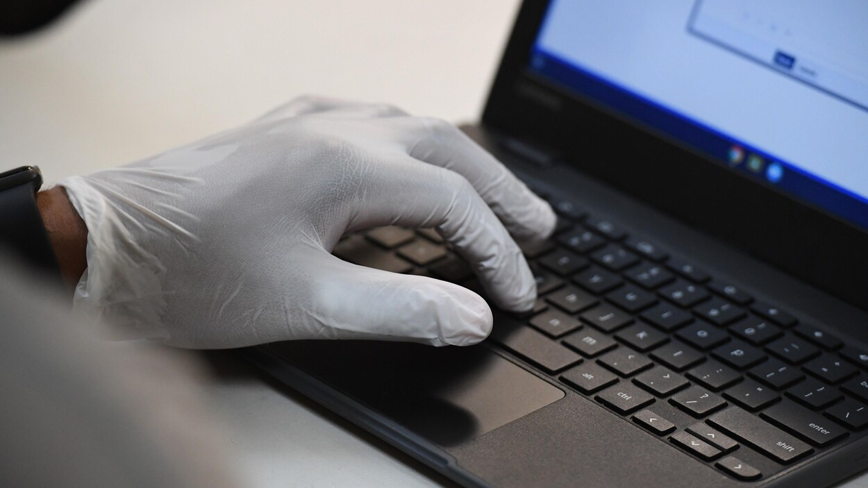 Une personne portant des gants de plastique utilise un ordinateur portable.