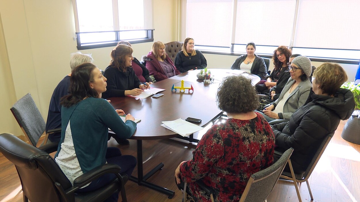 12 femmes assises autour d'une table avec un pont miniature en bois au centre de la table.
