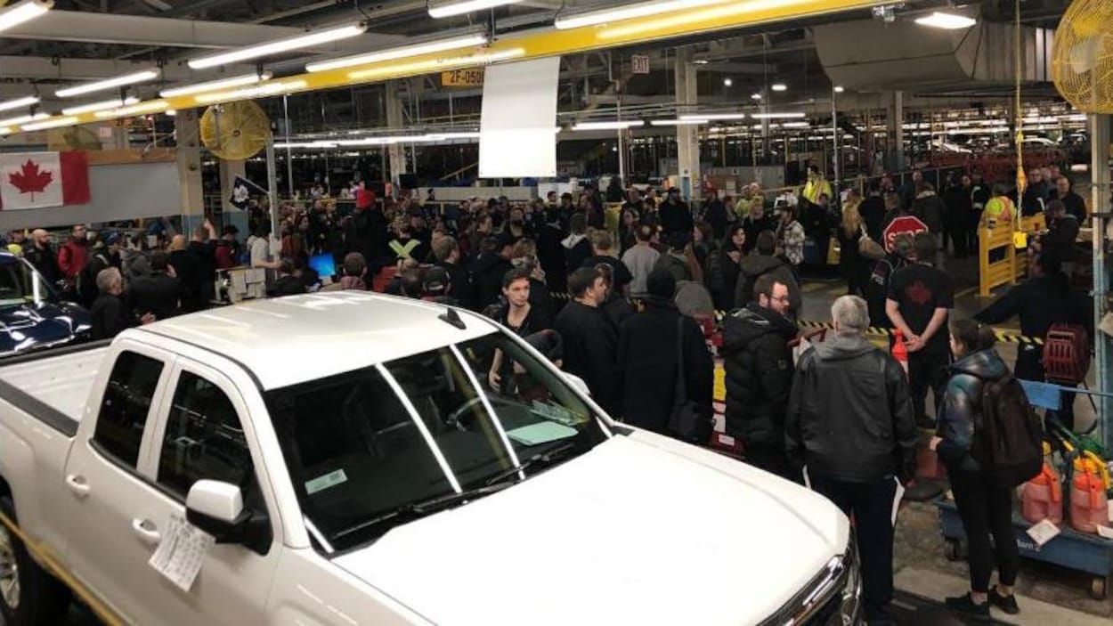 Un véhicule au premier plan, des employés dans une usine à l'arrière.
