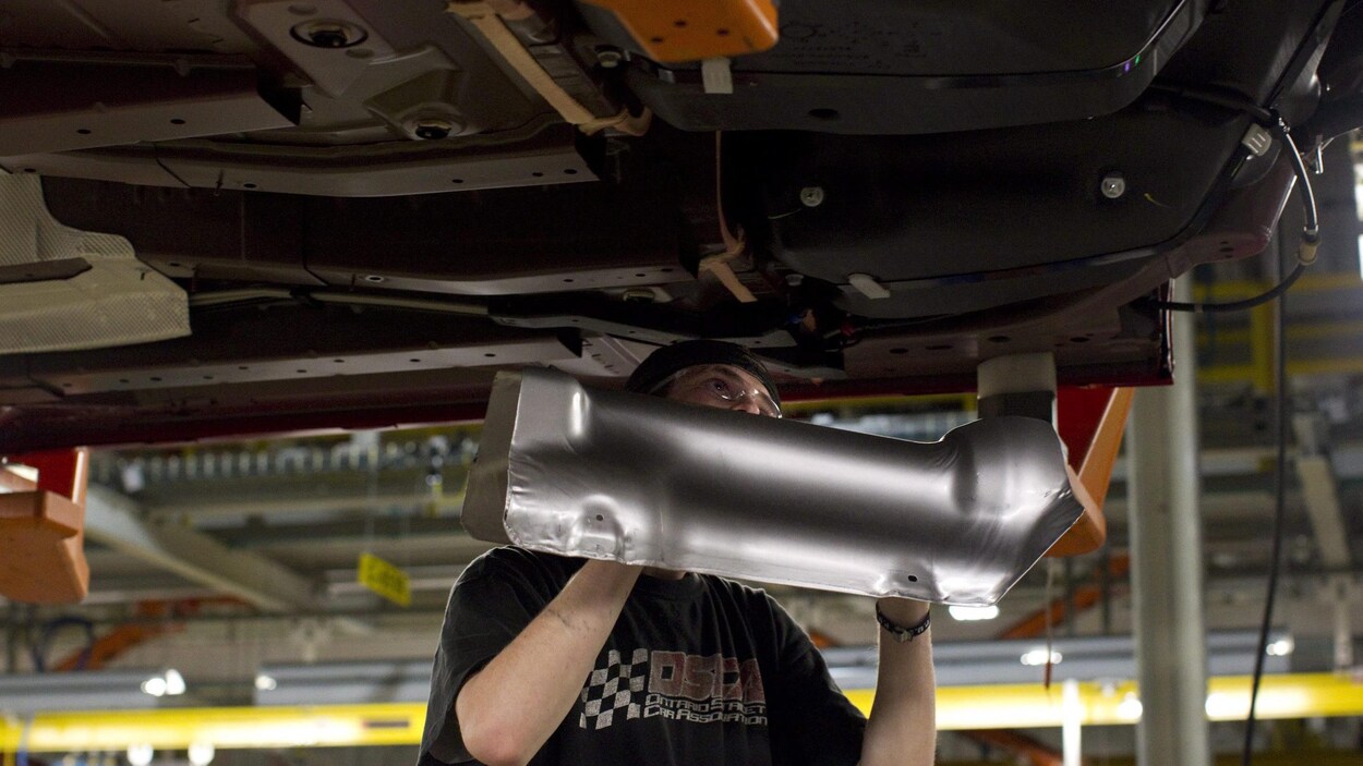 Un travailleur en train d'installer une pièce sous une automobile.