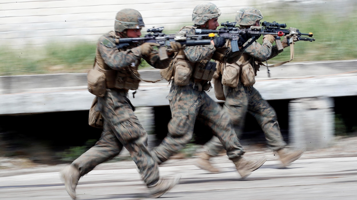 Trois soldats courent en pointant leur fusil d'assaut dans les rues d'un village en Lituanie.