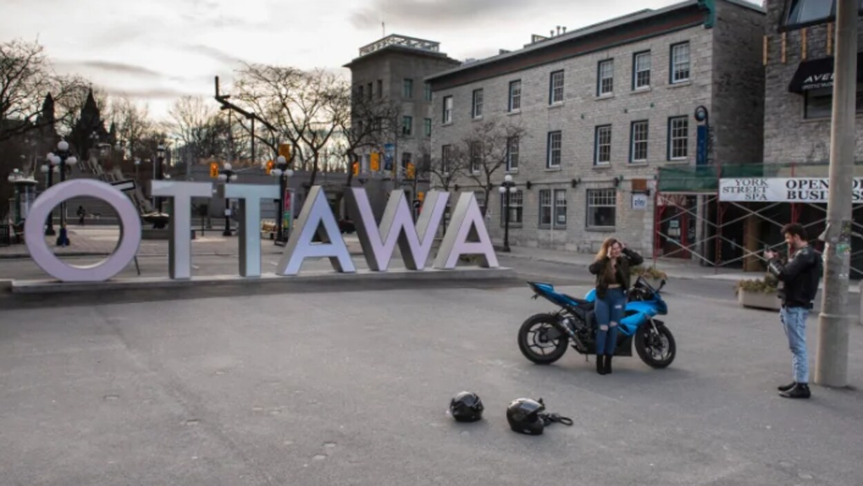 Deux personnes prennent des photos devant de grosses lettres en métal épelant le mot « Ottawa ».