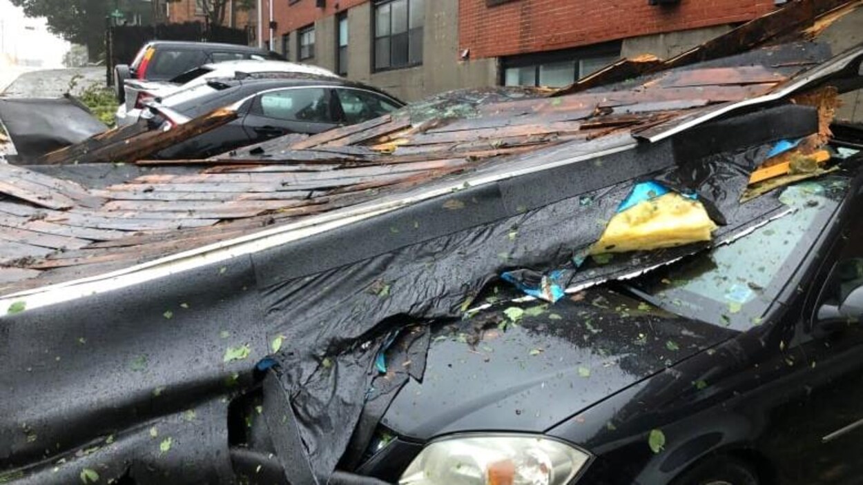 Des voitures sont écrasées par une toiture sous la pluie. 