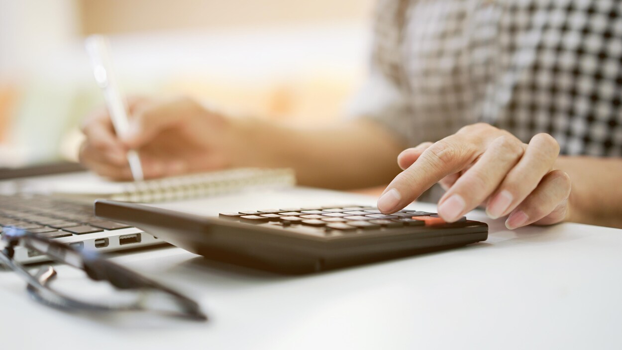 Gros plan sur la main d'une femme qui appuie sur une touche d'une calculatrice en faisant son budget.