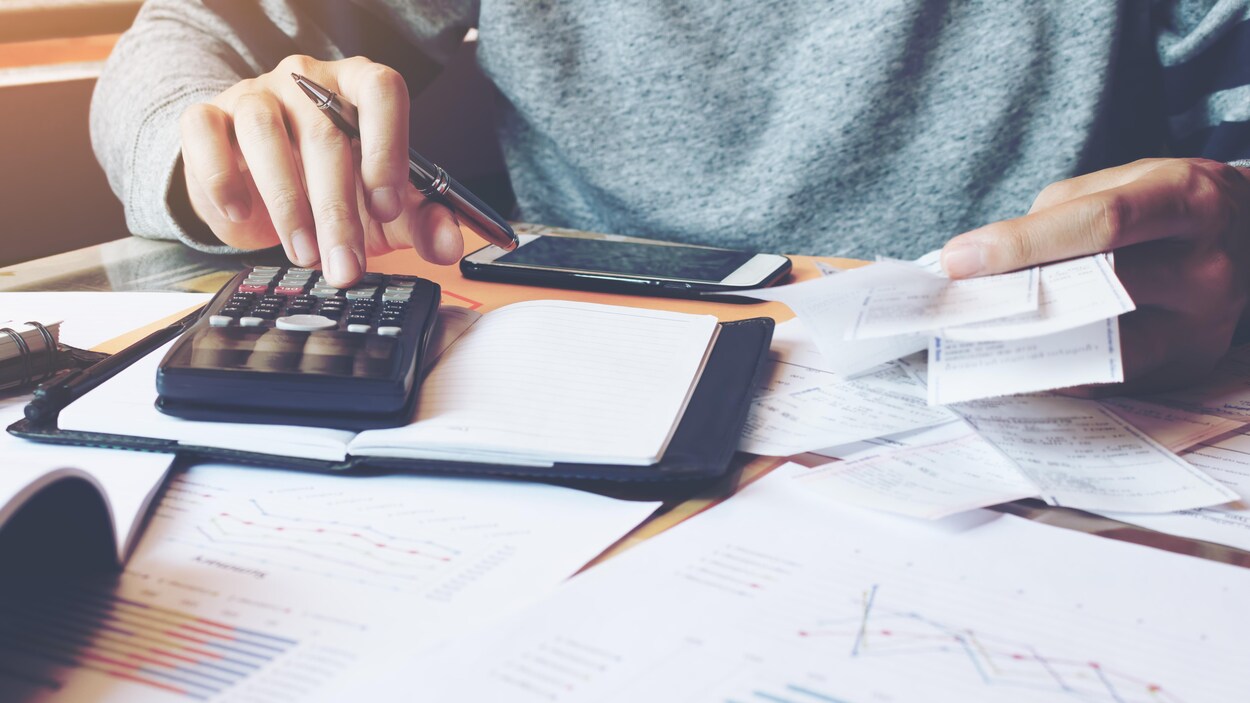 Ue personne utilisant une calculatrice et consultant ses factures. Ue personne utilisant une calculatrice et consultant ses factures.