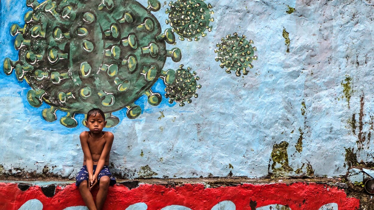 Un jeune garçon assis devant une murale représentant le coronavirus.