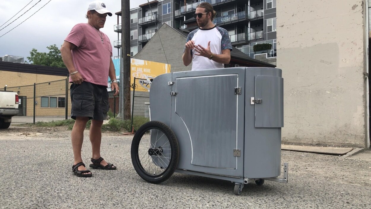 Deux hommes près du chariot gris métallique qui compte deux grandes roues à l'arrière et deux petites à l'avant. Deux hommes près du chariot gris métallique qui compte deux grandes roues à l'arrière et deux petites à l'avant.