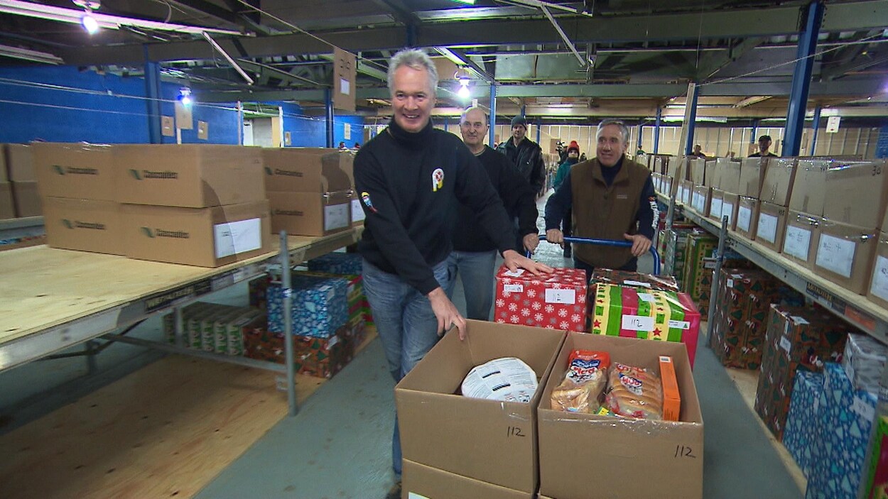 Des pompiers de Montréal poussent un chariot rempli de cadeaux et de paniers de Noël qu'ils ont préparés dans un de leurs entrepôts.