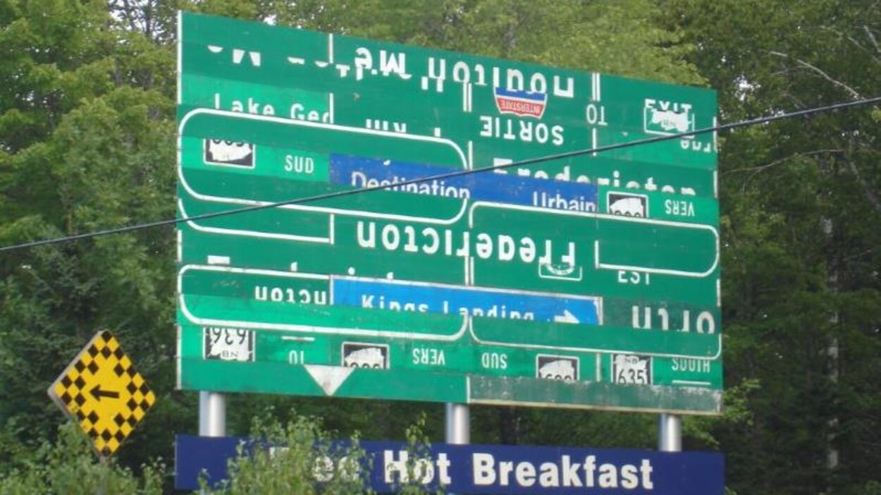 Un panneau routier vert composé de fragments de mots et d'affiches.