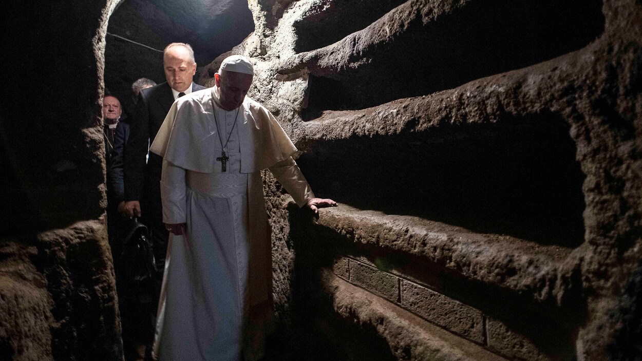 Le pape François marche en s'appuyant sur une tombe dans une catacombe.