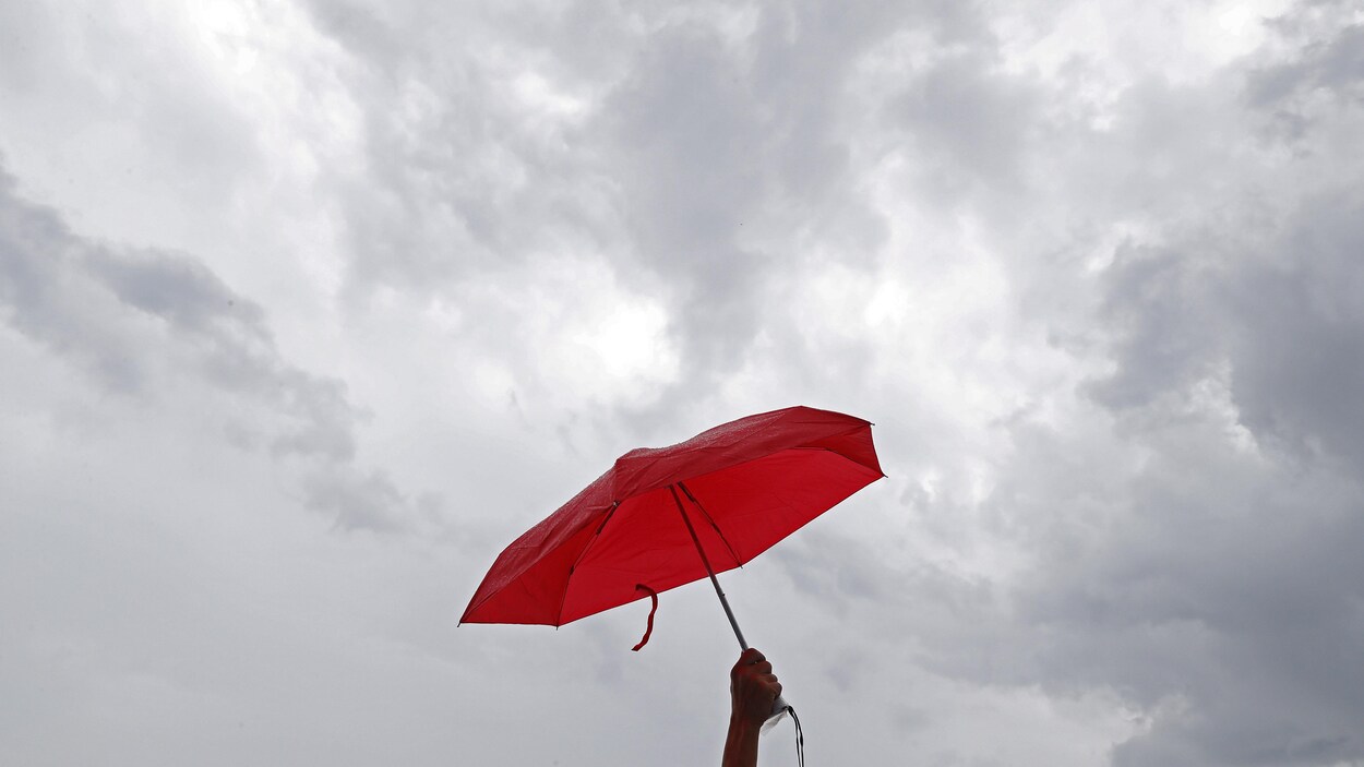 Une main tient un petit parapluie rouge.