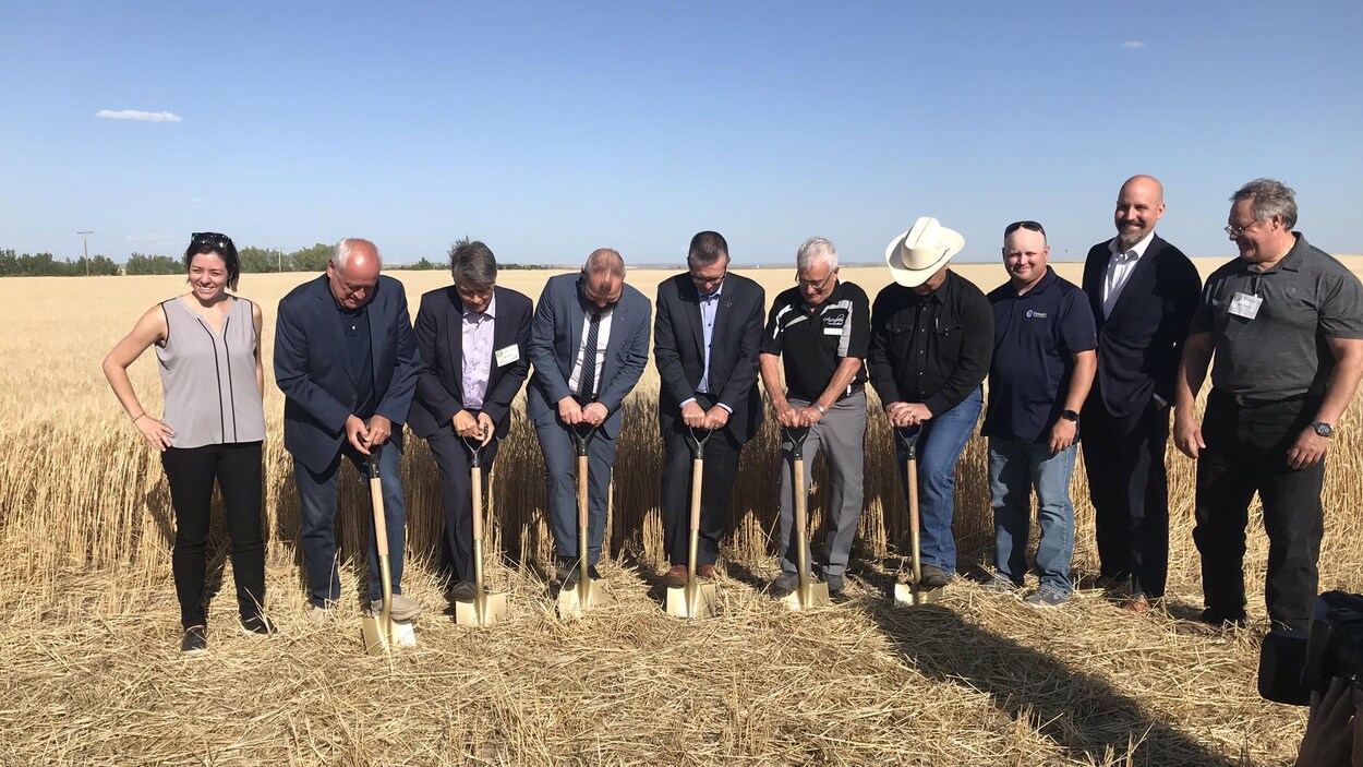 Des hommes donnent la première pelletée de terre dans un champ pour symboliser le début de la construction du parc éolie près d'Assiniboia. D'autres personnes se tiennent à côté d'eux.