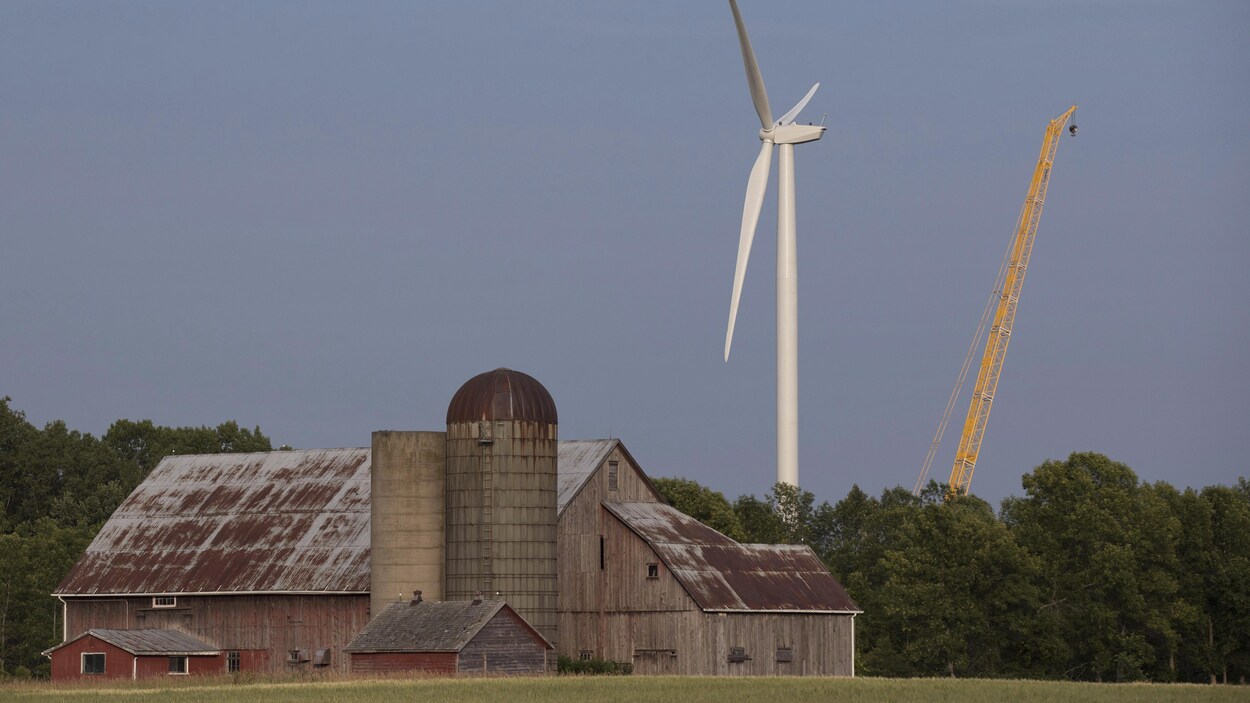Une éolienne et une grue derrière une grange.