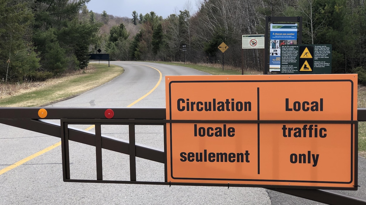 Une barrière indiquant que seule la circulation locale est permise sur une route asphaltée qui traverse une zone boisée du parc de la Gatineau.
