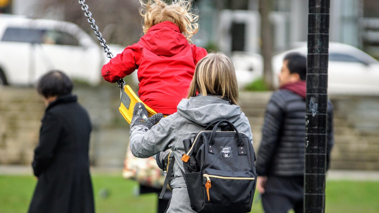 Une maman pousse son enfant sur une balançoire dans un jardin public de Vancouver.