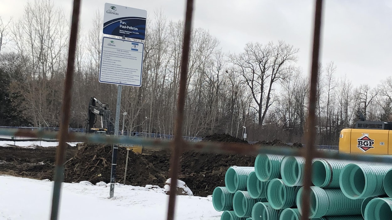Des excavatrices et des tuyaux verts sont placés sur le sol du parc Paul-Pelletier, derrière une clôture métallique.