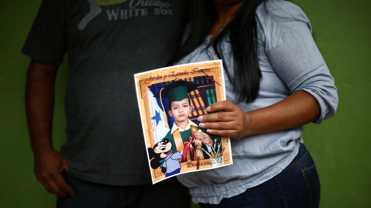 Un couple dont on ne voit pas le visage; la femme tient une photo d'école de son fils.