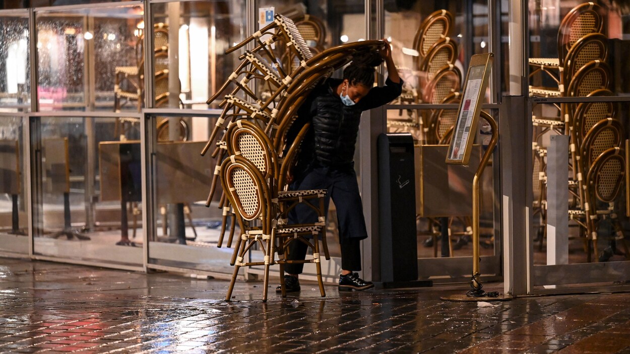 Une femme portant une pile de chaises sur une terrasse.