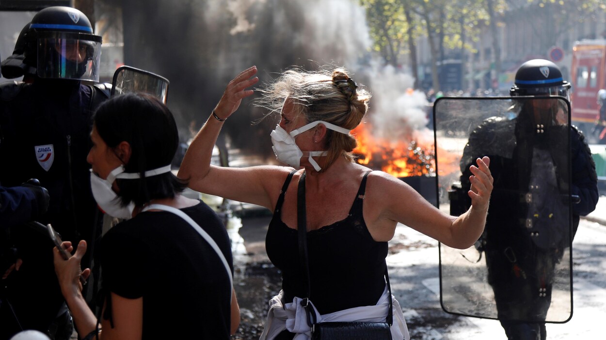 Deux policiers antiémeute et deux manifestantes, avec en arrière-plan un feu allumé dans la rue.