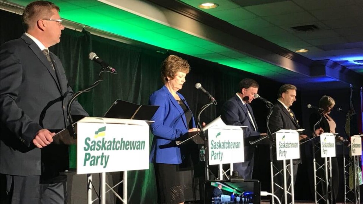 Les cinq candidats sur une scène côte à côte devant leur micro. Les cinq candidats sur une scène côte à côte devant leur micro.