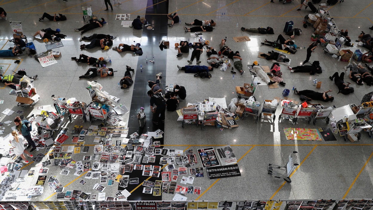 Des gens attendent, certains couchés sur le sol de l'aéroport.