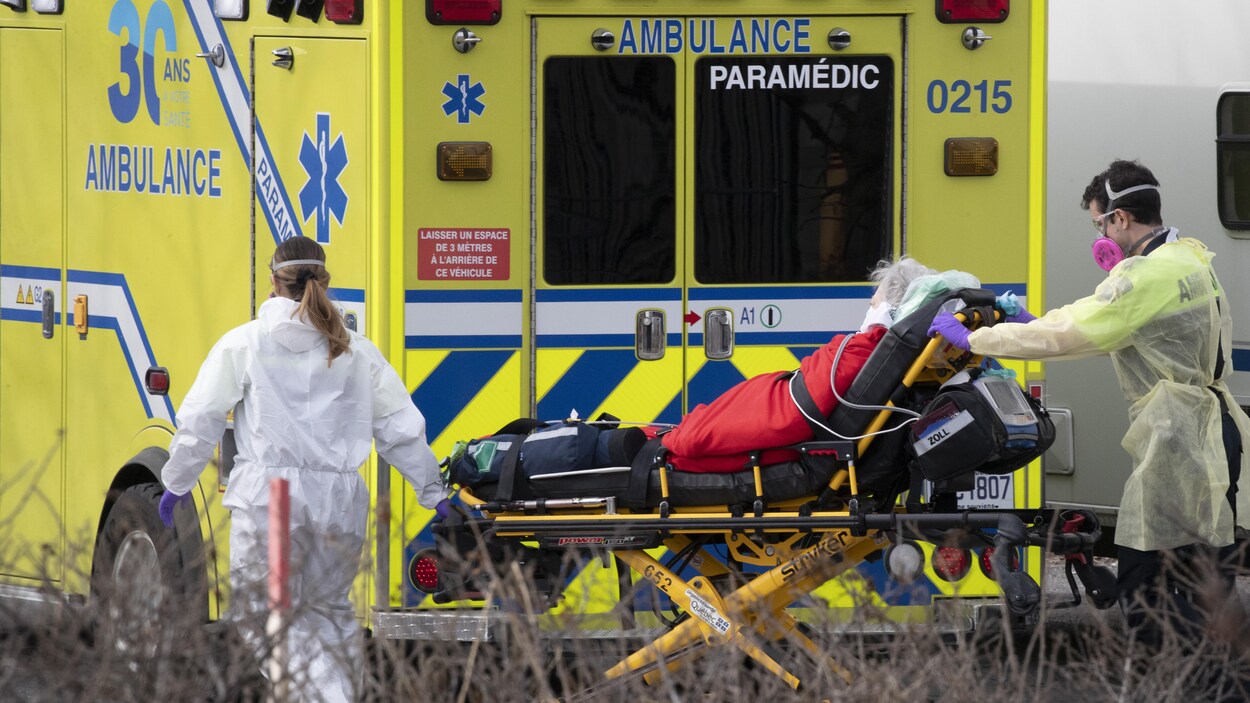 Un patient allongé et transporté par deux ambulanciers.
