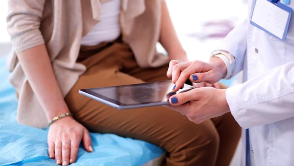 Une femme assise sur une table avec un professionnel de la santé qui tient un Ipad.