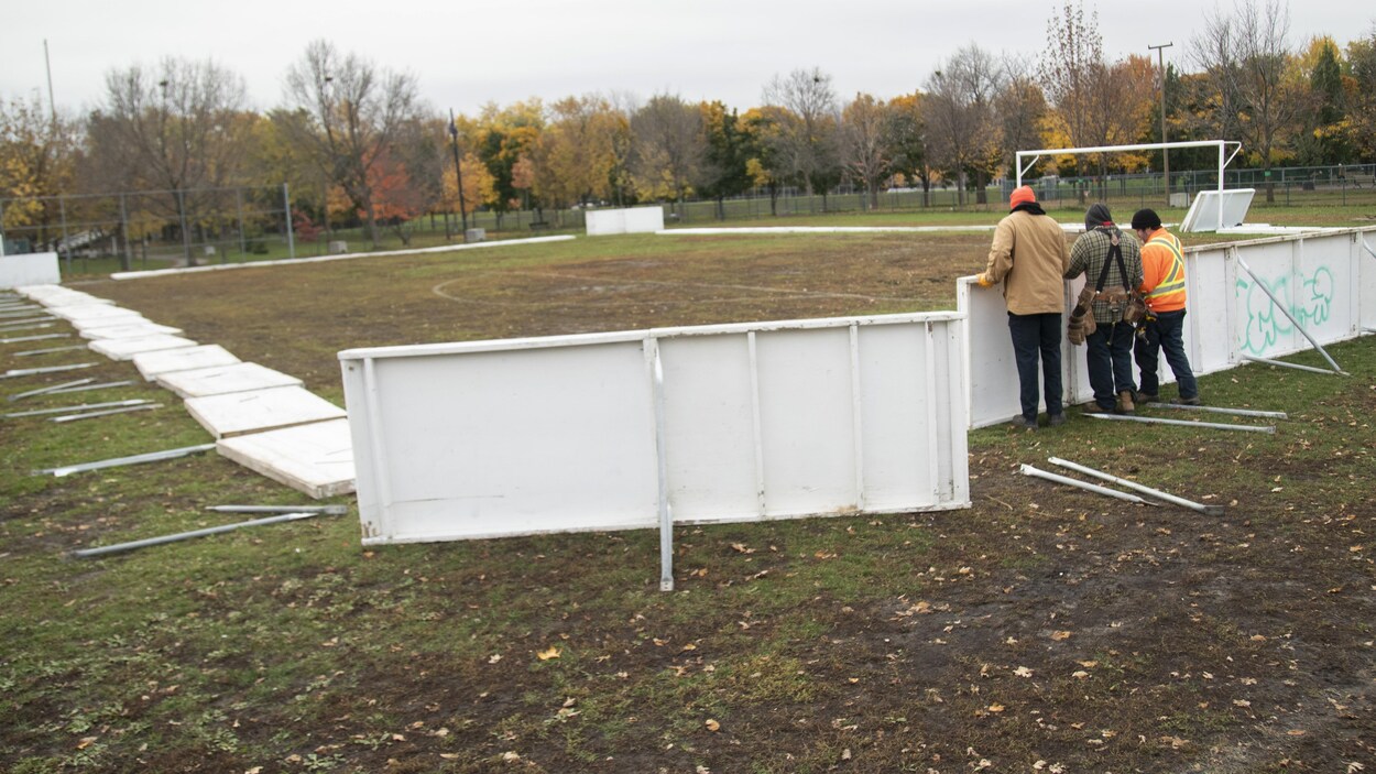 Des préposés installent les rampes pour monter une patinoire extérieure dans un parc.