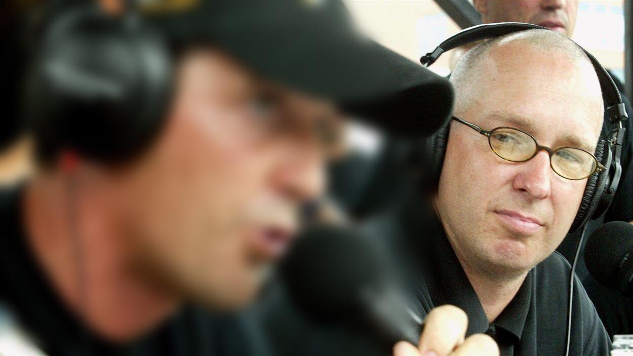Patrice Demers avec de petites lunettes rondes et un polo noir. Il porte un casque d'écoute.