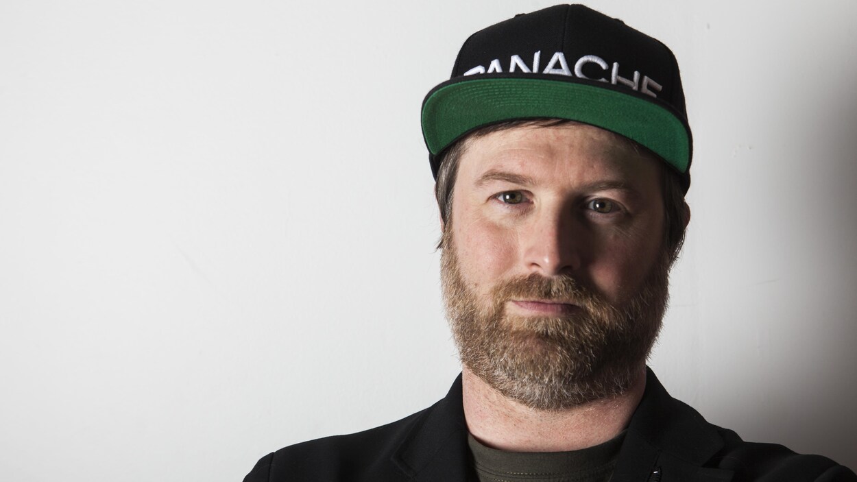 Une photo montrant Patrice Désilets. Il porte une casquette noire sur laquelle est brodé le mot Panache en blanc.