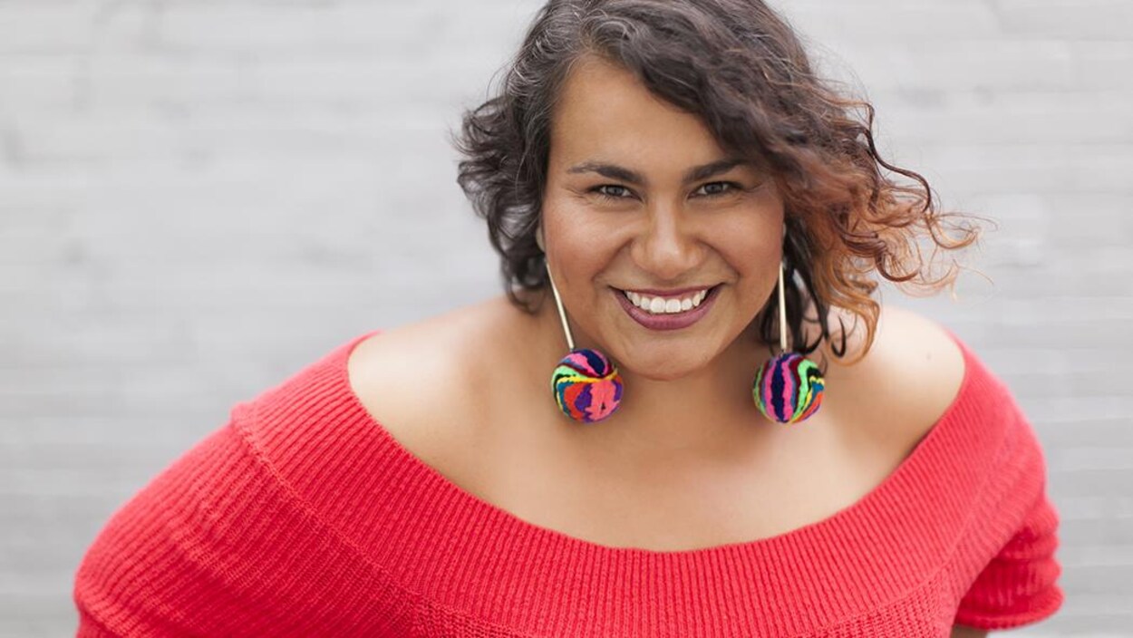 Patricia Cano porte un pull-over rouge, des boucles d'oreilles multicolores, elle a les cheveux ondulés bruns Patricia Cano porte un pull-over rouge, des boucles d'oreilles multicolores, elle a les cheveux ondulés bruns
