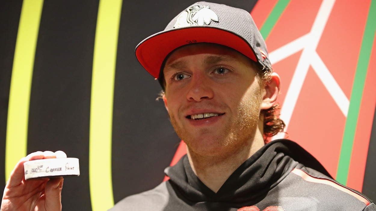 Devant un logo des Blackhawks, il montre la rondelle de son 1000e point aux photographes.