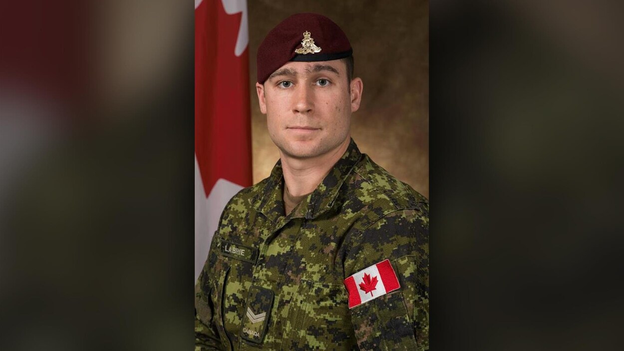 Le bombardier Patrick Labrie pose devant un drapeau canadien.